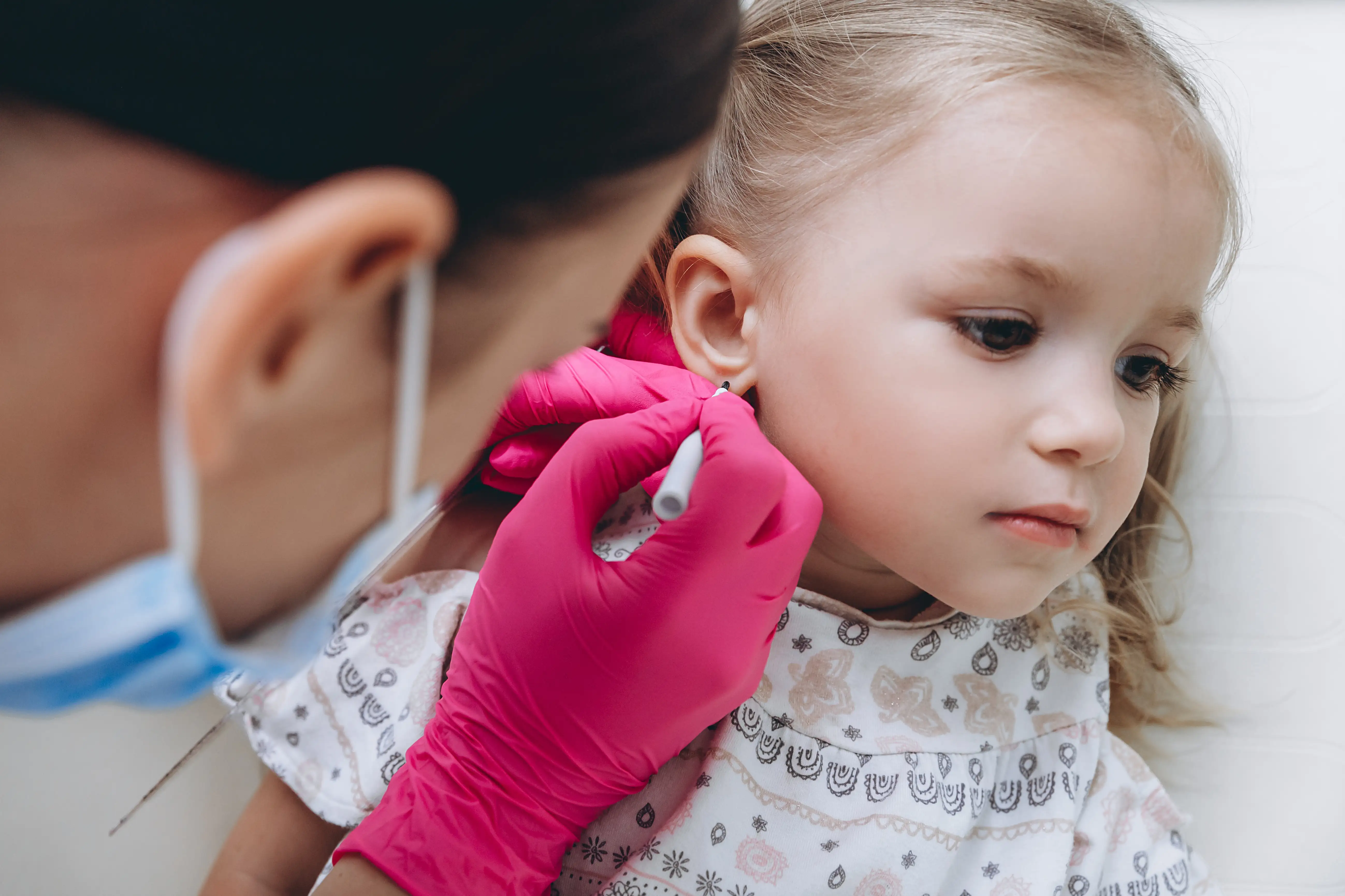 Gloved piercer marking a young child's earlobe